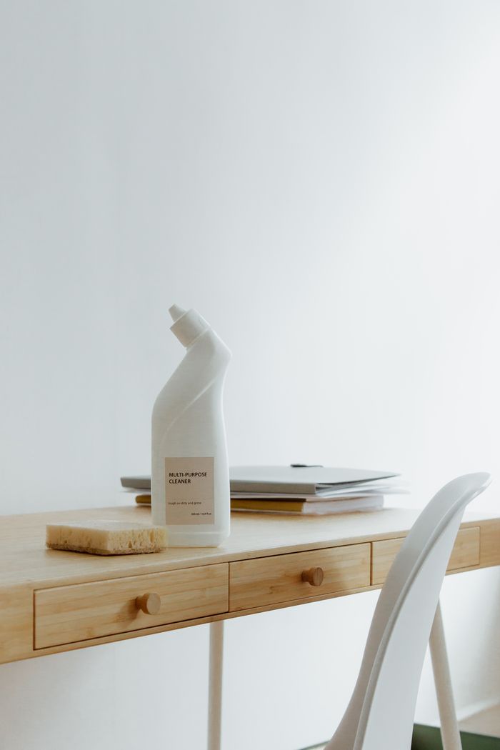 Un bureau de travail propre et organisé à la maison avec une bouteille de nettoyant et une éponge, soulignant la simplicité et la fonctionnalité.