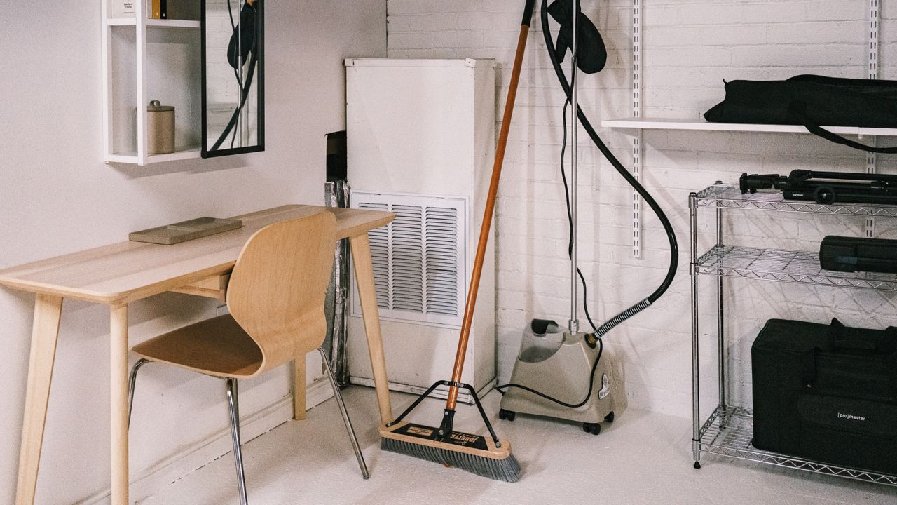 A tidy home office space featuring a wooden desk, chair, broom, and cleaning equipment.